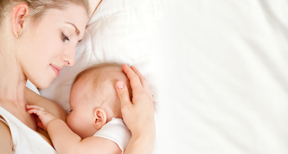 A woman is lying down, cradling a baby close to her chest.