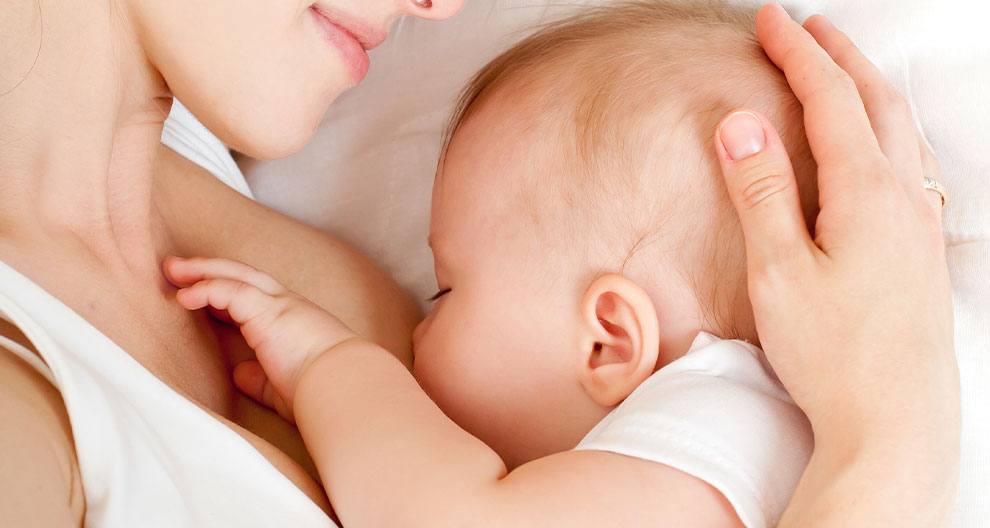 A close-up of a woman's face and hand, gently touching a baby's head.