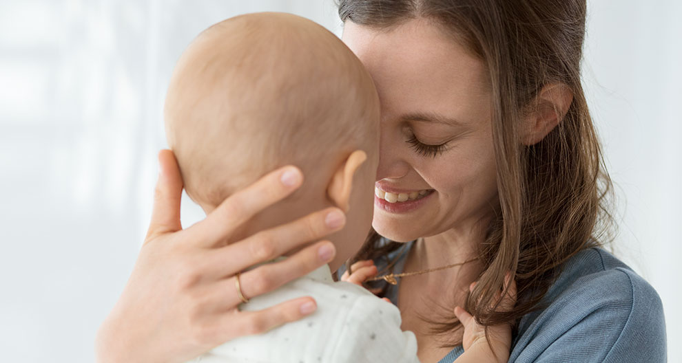 A woman in a blue shirt is holding a baby close to her face, with their foreheads touching.