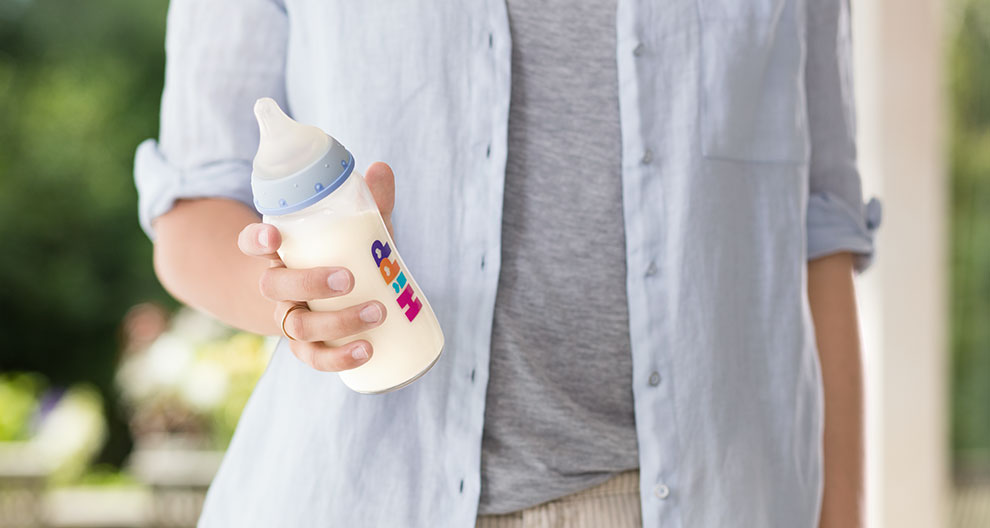 A person in a light blue shirt holds a baby bottle with a colorful label.