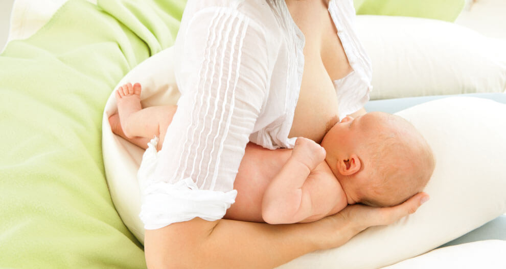 A woman in a white shirt is breastfeeding a baby.