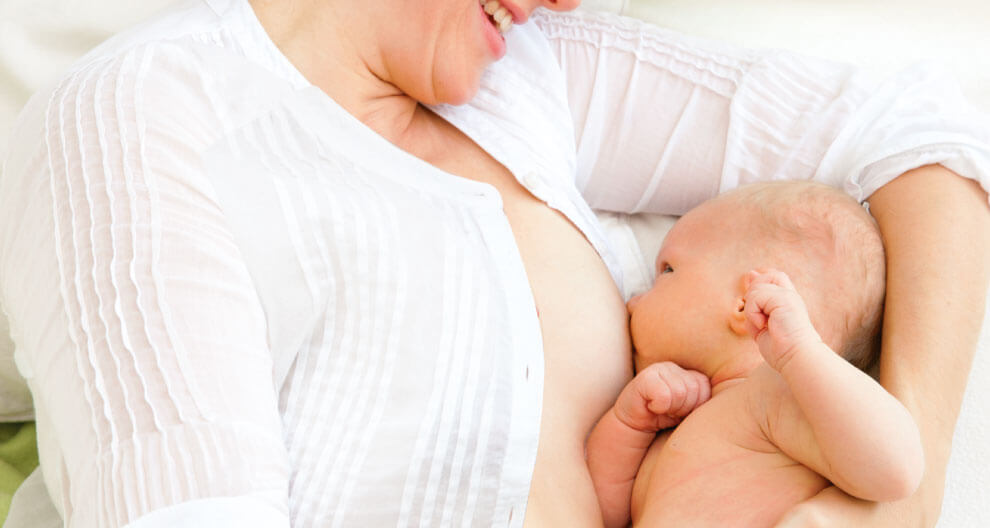 A woman in a white shirt is breastfeeding a baby.