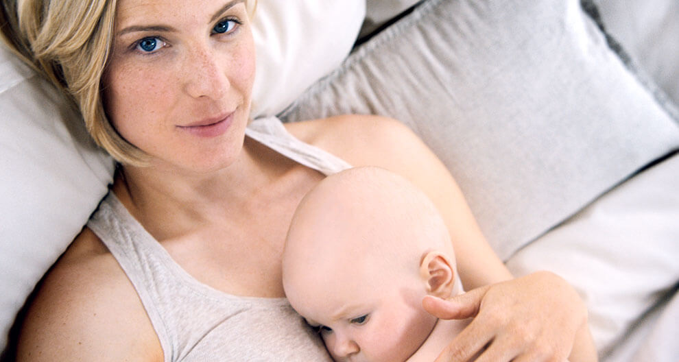 A woman in a white tank top is holding a baby.