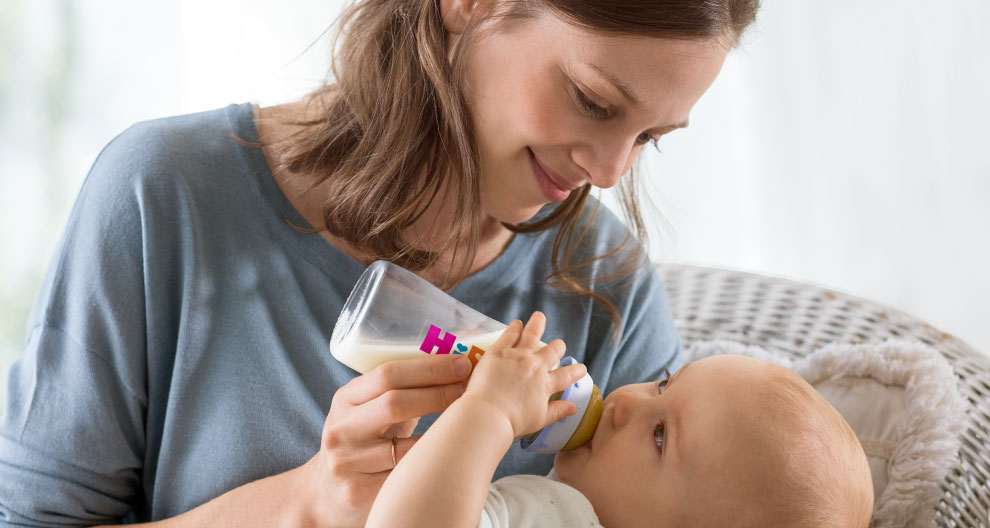 A woman in a blue shirt is feeding a baby with a bottle.