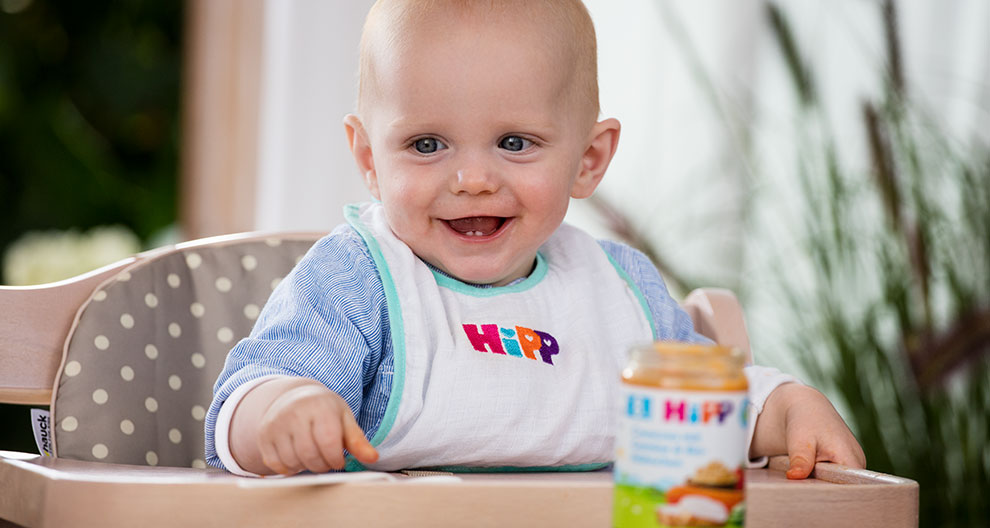 A baby in a high chair with a jar of food.