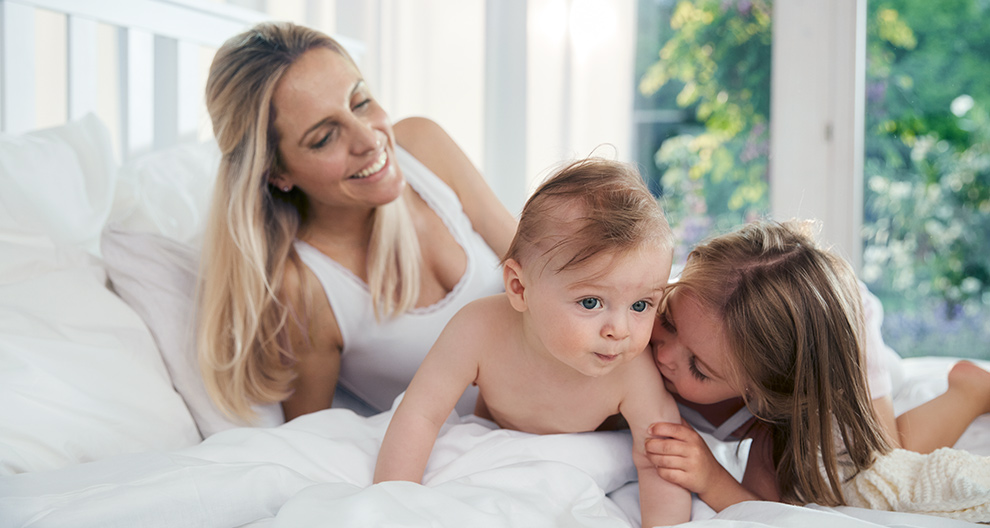 A woman and two children are engaged in a playful interaction on a bed.