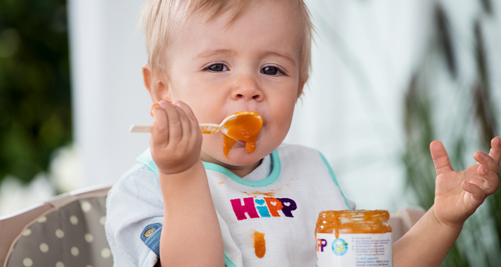 A toddler is eating from a jar with a spoon.