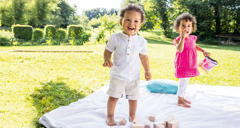 Two children play on a blanket in a grassy area.