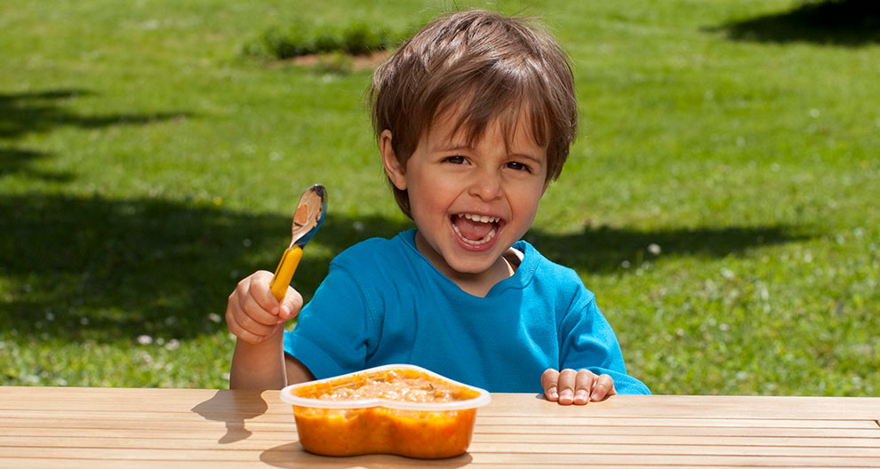 A child in a blue shirt is excitedly eating from a container with a spoon.