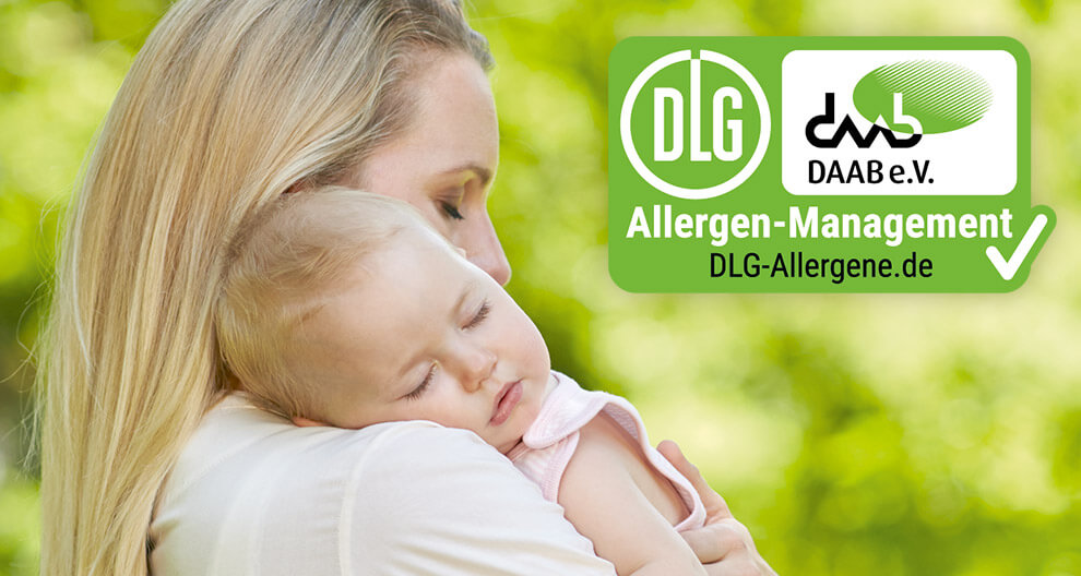 A woman holds a sleeping baby against a green background, with a DLG-Allergene.de logo superimposed.