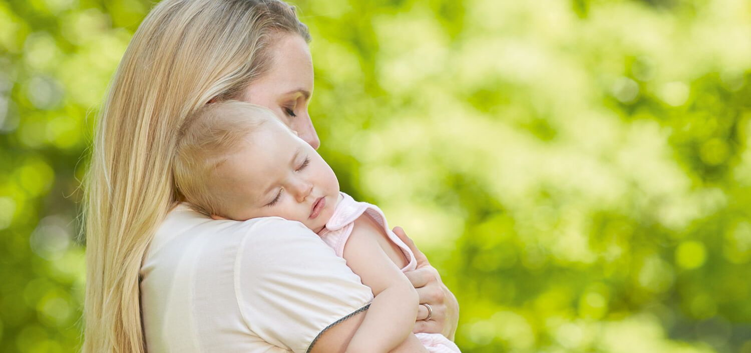 A woman holds a sleeping baby against a green background.