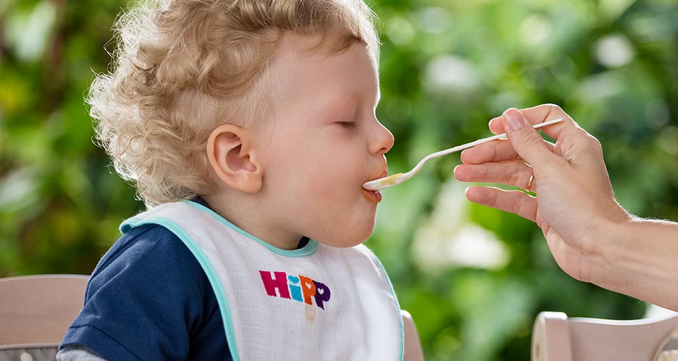 A child with curly hair is being fed with a spoon.