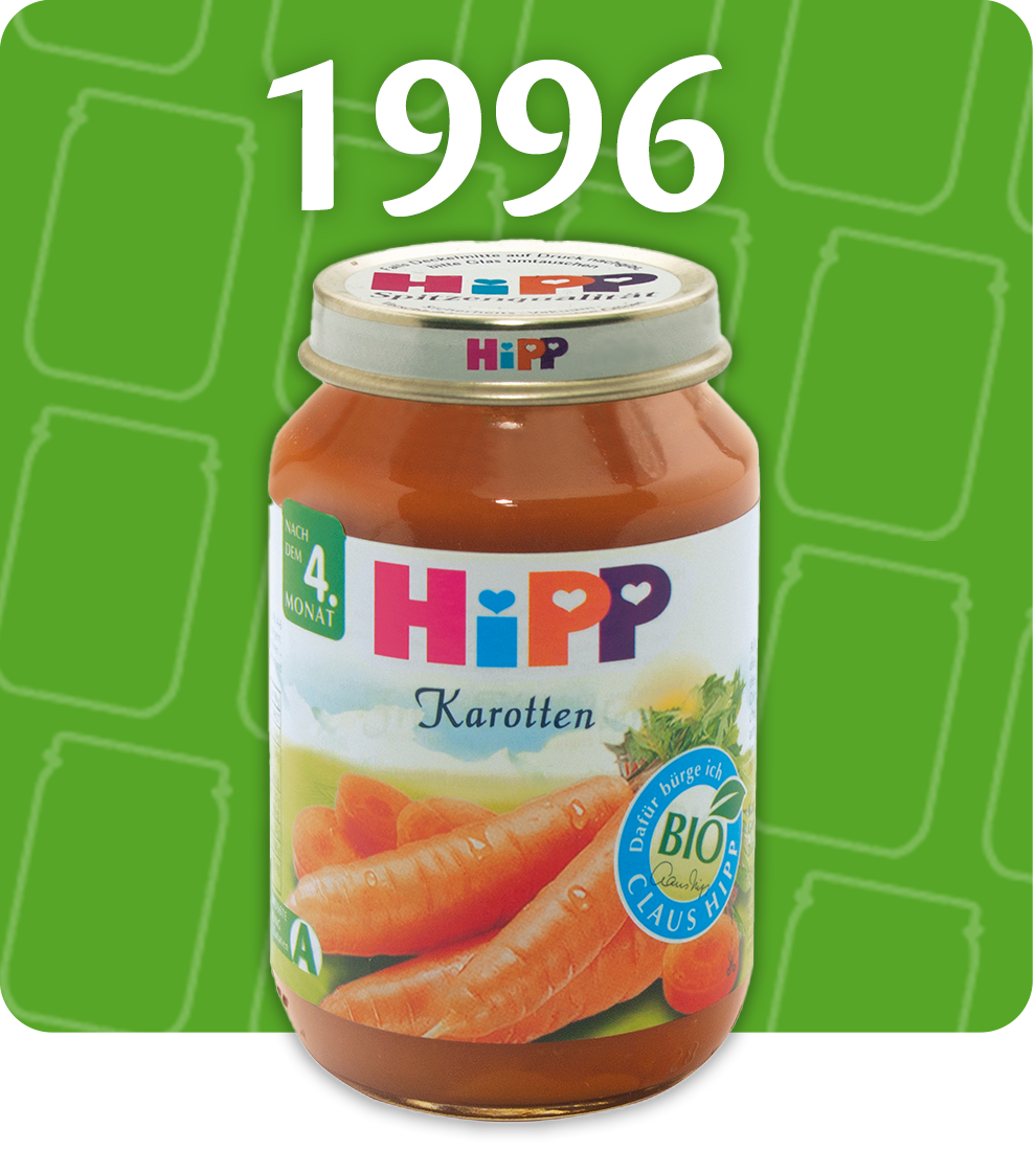 A jar of Hipp baby food with carrots, labeled as organic, is presented against a green background with the year 1996 displayed above.