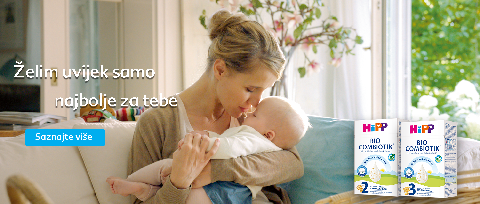Majka s ljubavlju drži svoju bebu, dok je u pozadini reklama za proizvod "HiPP BIO COMBIOTIK".