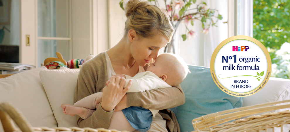 Žena s ljubavlju drži bebu, s logom koji promovira organsku mliječnu formulu u pozadini.