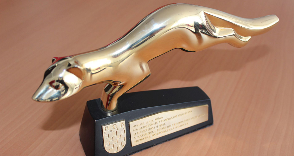 Zlatna, zamršeno dizajnirana statua životinje u skoku postavljena je na crno pravokutno postolje sa štitnim amblemom i natpisima.