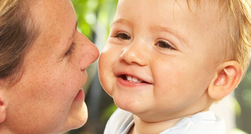 Krupni plan žene i bebe, s djelomično vidljivim licem žene i potpuno vidljivim licem bebe, kako se gledaju.
