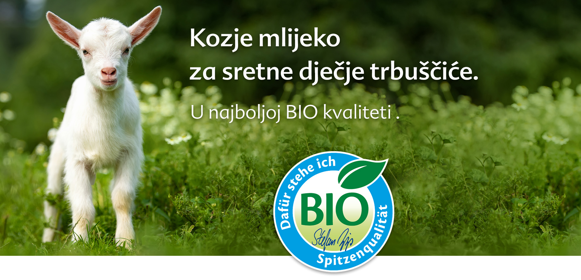 Bijela koza stoji na bujnom zelenom polju s plavo-bijelim bio logotipom u prvom planu.