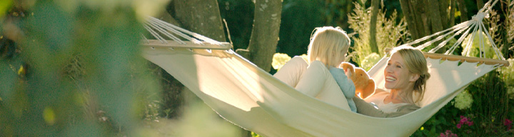 Dvoje ljudi leže u visećoj mreži, okruženi drvećem i biljkama.