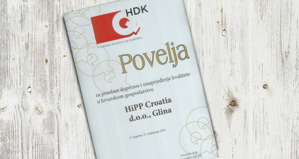 Bijeli certifikat s crvenim i crnim tekstom, na kojem se nalazi logotip HDK-a, postavlja se na drvenu površinu.