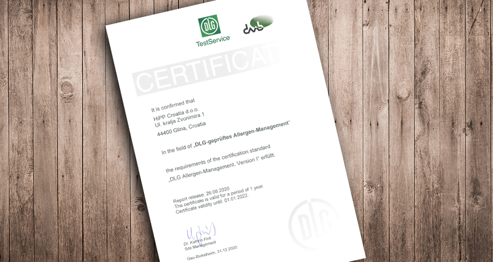 Bijeli certifikat sa zelenim i crnim tekstom pričvršćen je na drvenu površinu, a na dnu se nalazi logotip DLG-a, TestService i potpis.