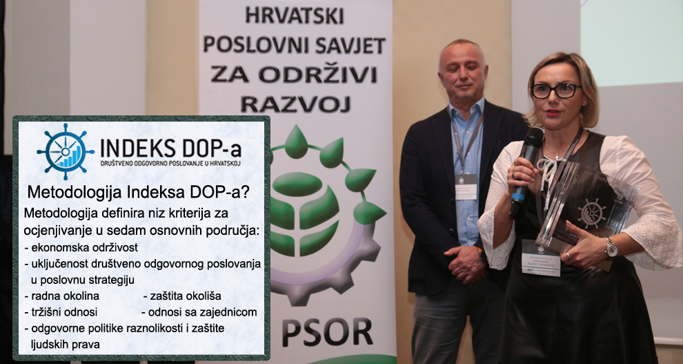Žena s naočalama drži mikrofon i prozirnu nagradu, stoji pored muškarca u odijelu, ispred bijelog transparenta s tekstom i logotipom, sa zeleno-bijelom informativnom pločom s lijeve strane.