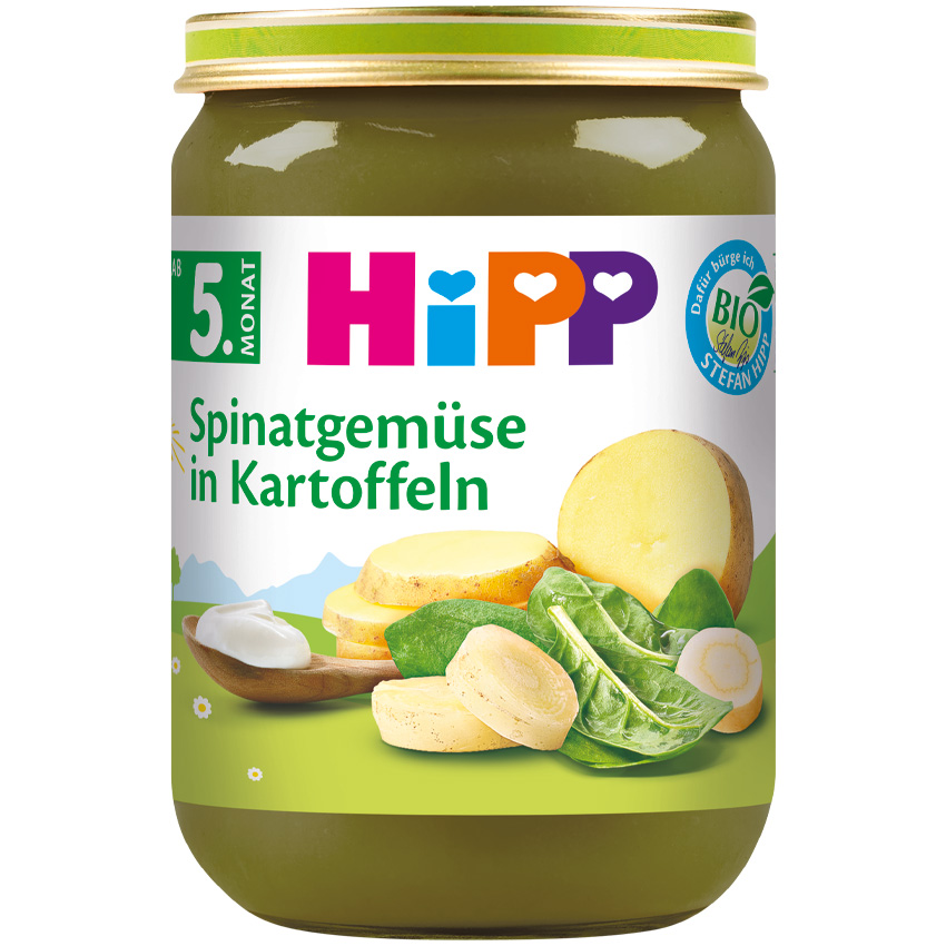 Staklenka dječje hrane s etiketom na njemačkom jeziku, na kojoj su krumpir i špinat, uz drvenu žlicu s malo hrane i nekim sirovim sastojcima.